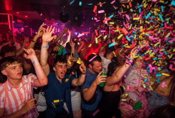 Tramps Tenerife nightclub packed with partygoers dancing under red and purple lights as colourful confetti fills the dance floor.
