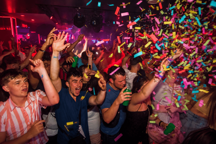 Tramps Tenerife nightclub packed with partygoers dancing under red and purple lights as colourful confetti fills the dance floor.